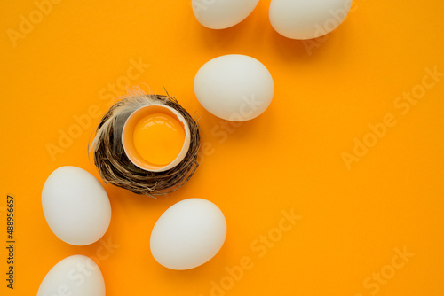 White eggs and egg yolk into nest on yellow background. Top view. Flat lay. Easter celebration photo