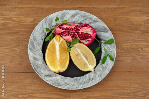Ripe fruits of yellow orange and pomegranate . on a black and white plate. Citrus fruits on a platter. Still-life. on a wooden background. top view. close-up.