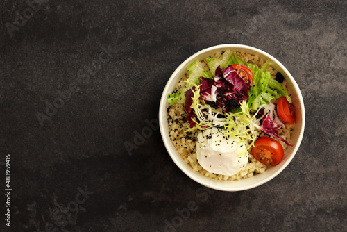 Healthy bowl with poached egg, bulgur, tomatoes and lettuce. on a dark background in an eco paper box. Healthy food delivery concept.