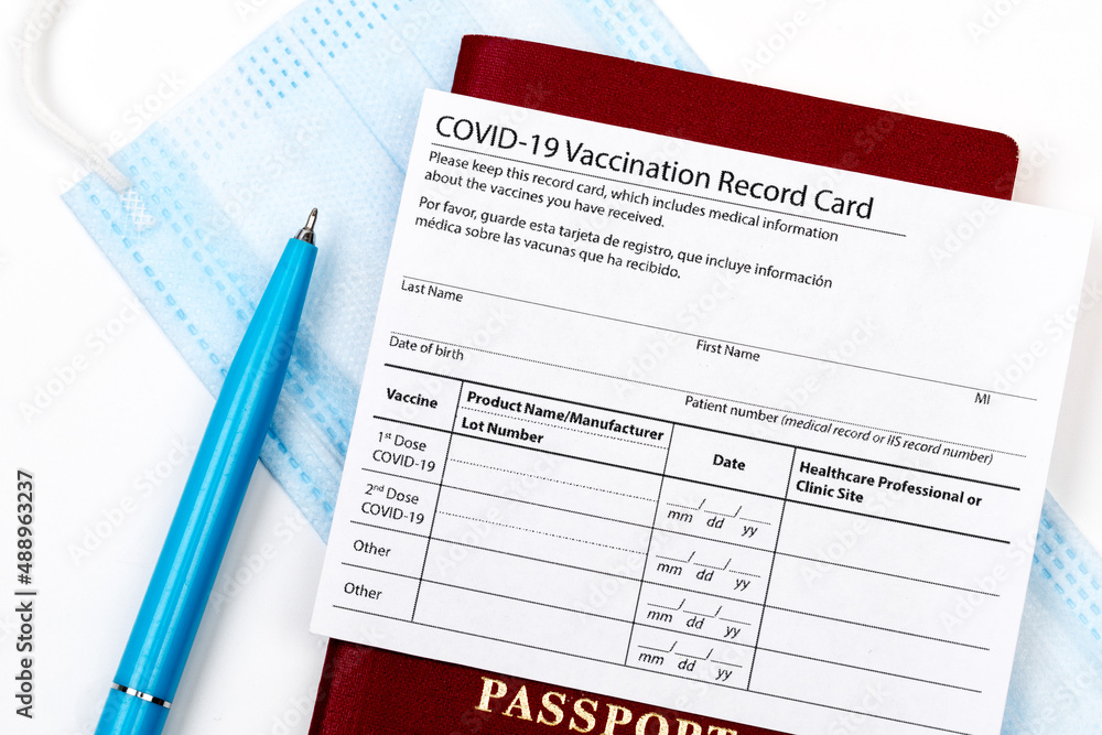 Obraz premium Coronavirus vaccination record card, biometric passport and blue medical mask on light gray desk. Concept of defeating Covid-19. Vaccination as prerequisite for travel - Image
