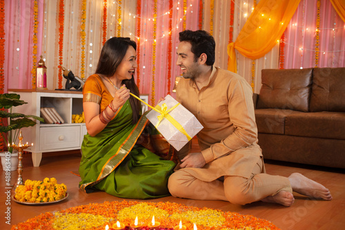 Young Indian couple - Happy husband gifting his wife on Diwali festival. 
Indian festival Diwali celebration at home - happy family, hindu festival, rangoli at home, colorful festival decoration, gift