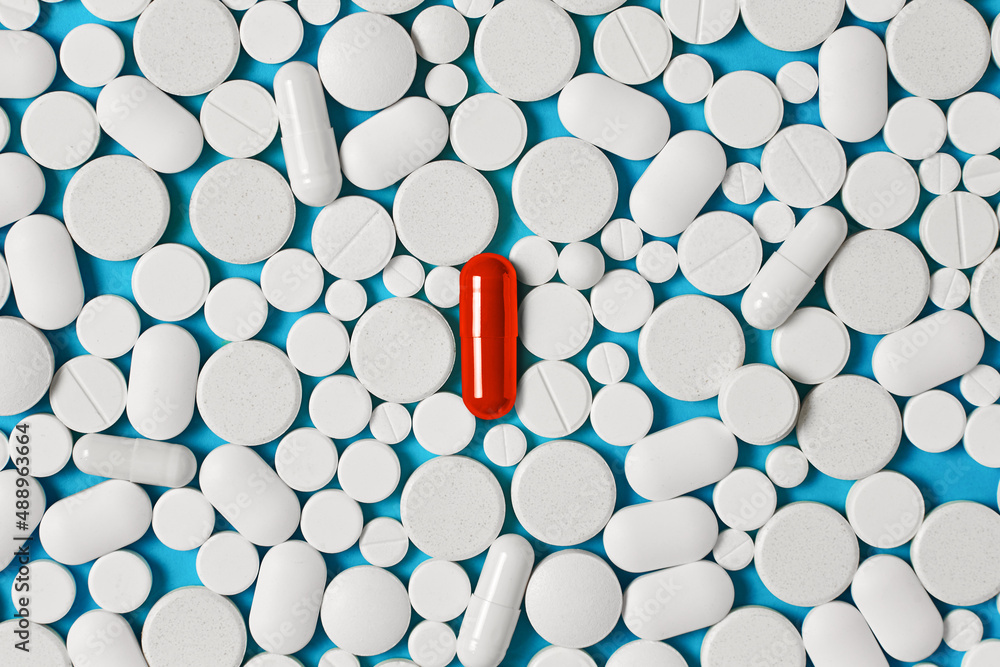 the concept of unusualness and eccentricity. Bright red pill on a background of a large number of colorless pills - obrazy, fototapety, plakaty 