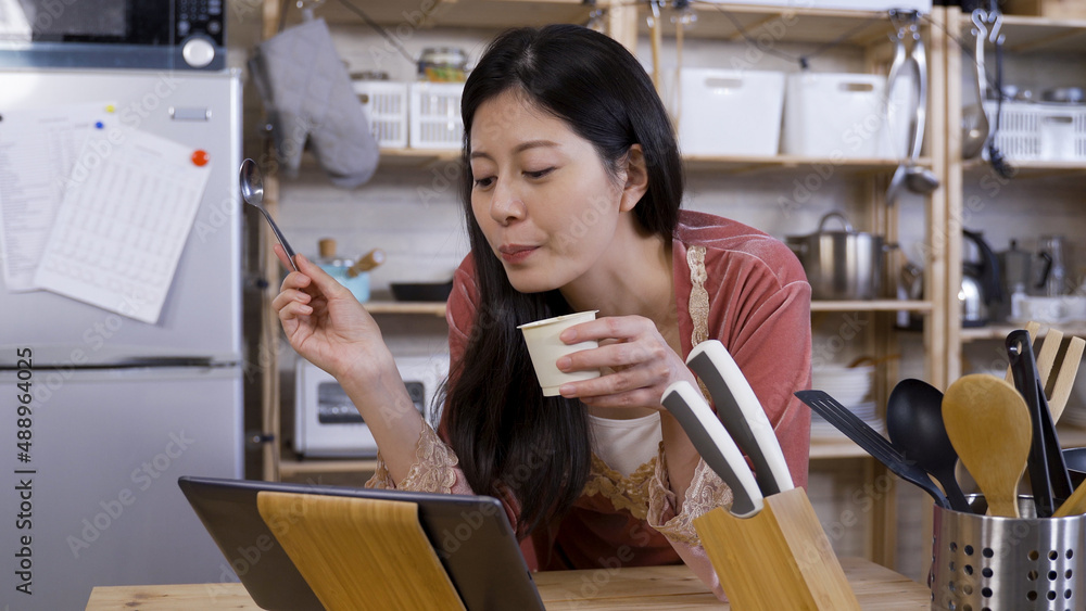 close up happy korean girl leaning over kitchen table is enjoying yogurt and watching social media posts with a touchpad close up happy korean girl leaning over kitchen table is enjoying yogurt and watching social media posts with a touchpad