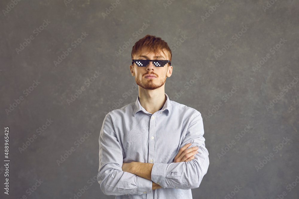 Haughty bearded film fan with pixel glasses, person with cross his arms, portrait, gray background. Sly young guy. Man stands, arms crossed. Cool man with glasses. Haughty bearded film fan with pixel glasses, person with cross his arms, portrait, gray background. Sly young guy. Man stands, arms crossed. Cool man with glasses.