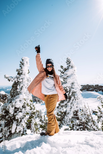 Russia. Sheregesh. Beautiful Girl in black sun goggles in winter in sunny weather outdoors among the Christmas tree and snow against blue sky. The girl is posing and smiling.