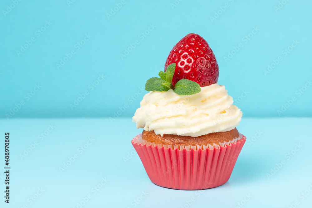 cupcake with whipped cream decorated strawberry and mint on blue background, minimalism concept