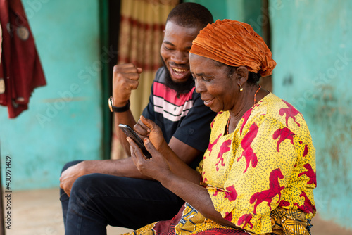 young african man and elderly woman looking at a phone rejoices
