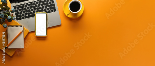 A top view of office flat lays (note books, smart phone, laptop and a cup of coffee) on an empty yellow-orange space on a background, for business and technology concept.