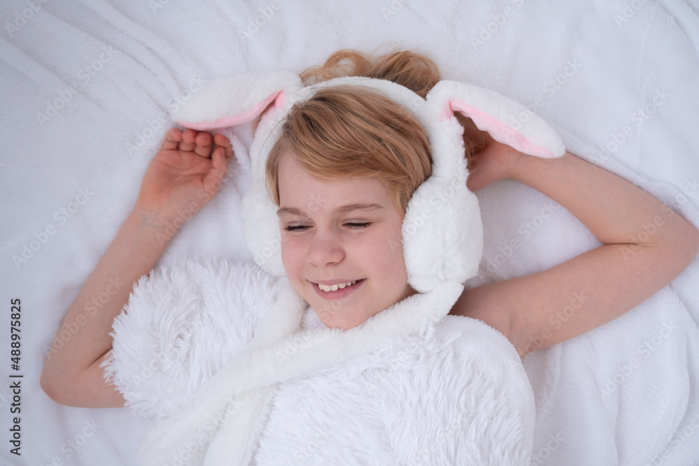 Beautiful little girl plays with rabbit ears. Easter concept. View from above. A child on a bed with a fluffy white blanket. Nice and cute picture Beautiful little girl plays with rabbit ears. Easter concept. View from above. A child on a bed with a fluffy white blanket. Nice and cute picture