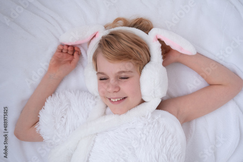 Beautiful little girl plays with rabbit ears. Easter concept. View from above. A child on a bed with a fluffy white blanket. Nice and cute picture