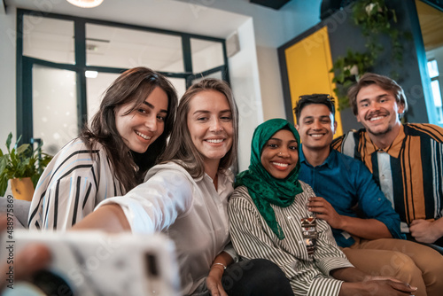 Group of business people during break from the work taking selfie picture while enjoying free time in relaxation area at modern open plan startup office. Selective focus  photo