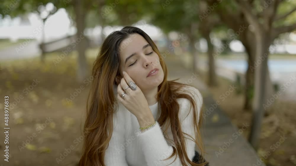 Close view of young brown-haired woman in park touching her face Close view of young brown-haired woman in park touching her face