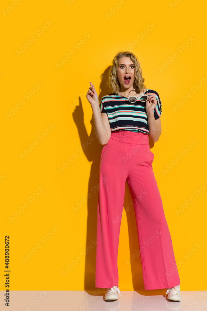 Excited young woman in pink oversized pants, sneakers and striped blouse is pointing up and talking Excited young woman in pink oversized pants, sneakers and striped blouse is pointing up and talking