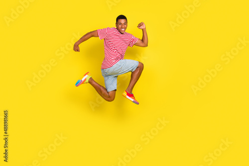 Full body profile side photo of guy jump run fast copyspace wear striped clothes color footwear isolated over shine yellow background