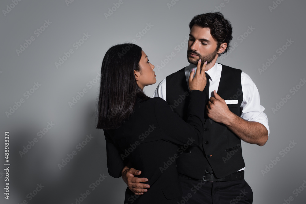 sensual asian woman touching face of stylish man on grey background
