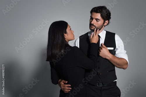 sensual asian woman touching face of stylish man on grey background