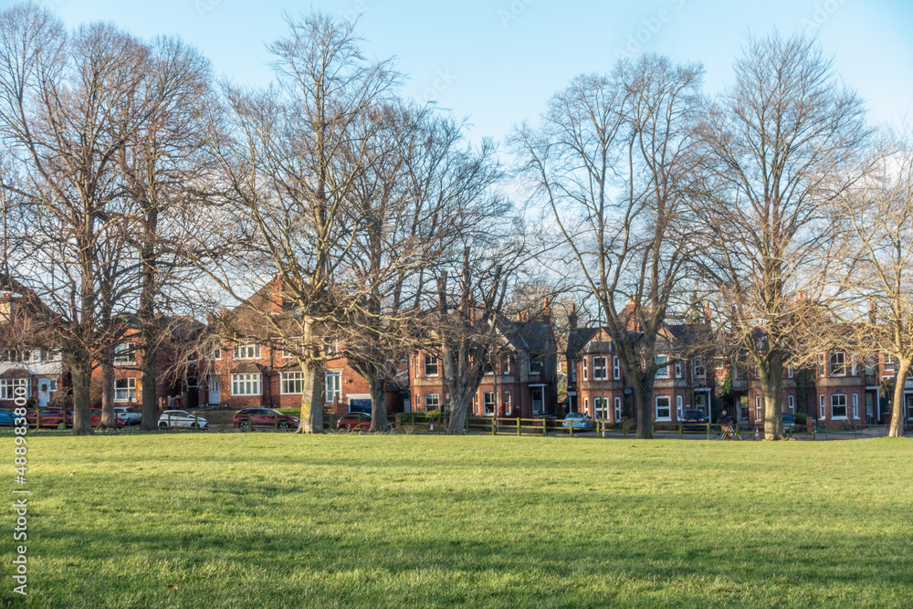 The edge of Prospect Park in Tilehurst, Reading, England lined with trees and houses opposite. The sky is blue and tree branches are bare. The edge of Prospect Park in Tilehurst, Reading, England lined with trees and houses opposite. The sky is blue and tree branches are bare.