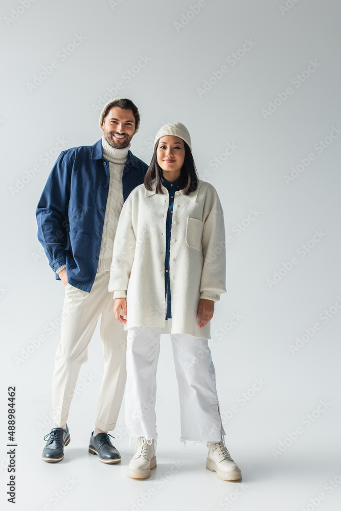 full length view of interracial couple in trendy white and blue clothes on grey background full length view of interracial couple in trendy white and blue clothes on grey background