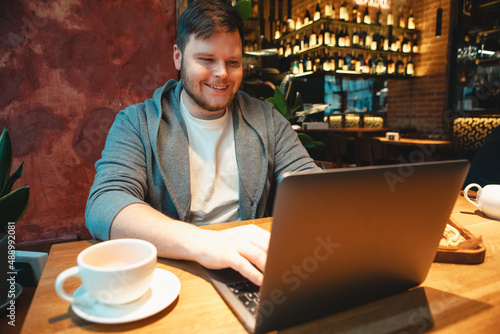 man freelancer working on laptop in cafe eating burger and drinking tea