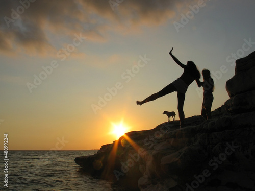 Fototapeta Naklejka Na Ścianę i Meble -  Female and dog silhouettes on seacoast against the sunset sky