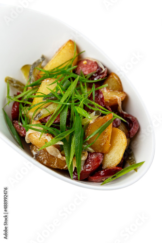 Potato salad with smoked sausages and green onions. Isolated on white background. Vertical.