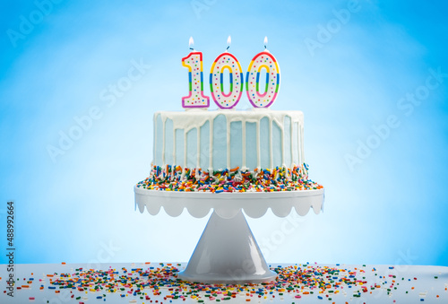 Blue Birthday Cake with Sprinkles on a White Cake Plate and Blue Background with 100 candles on Top