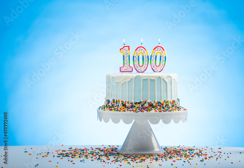 Blue Birthday Cake with Sprinkles on a White Cake Plate and Blue Background with 100 candles on Top