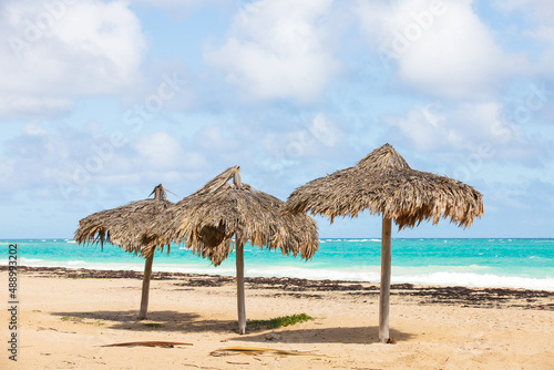 Three wooden umbrellas stand on an empty beach
