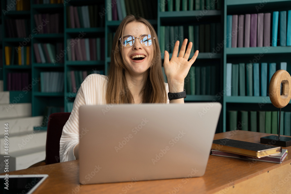 Workplace video communication manager uses laptop computer. Portrait of a female student with glasses in the office in the library. Workplace video communication manager uses laptop computer. Portrait of a female student with glasses in the office in the library.