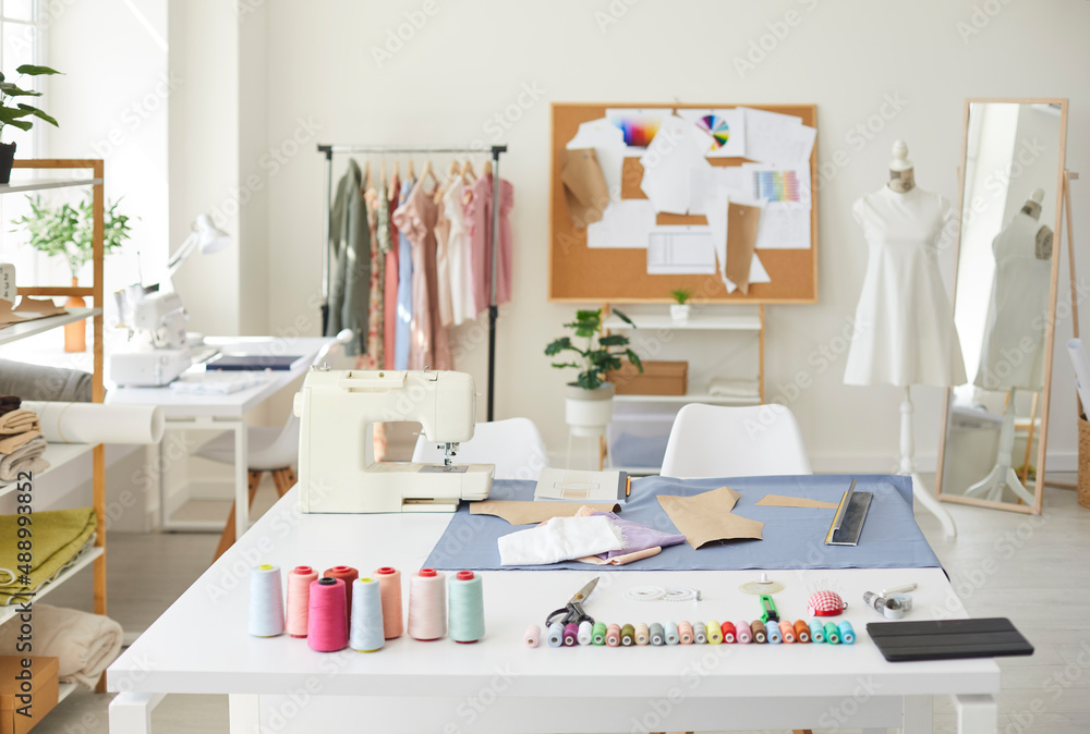 Empty fashion atelier of designer or seamstress with threads and sewing machine on table. No people in own stylish workshop of tailor or dressmaker. Clothing garment design. Style and dressmaking.