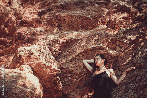 Girl in a black dress posing on a background of sand rocks. Portrait