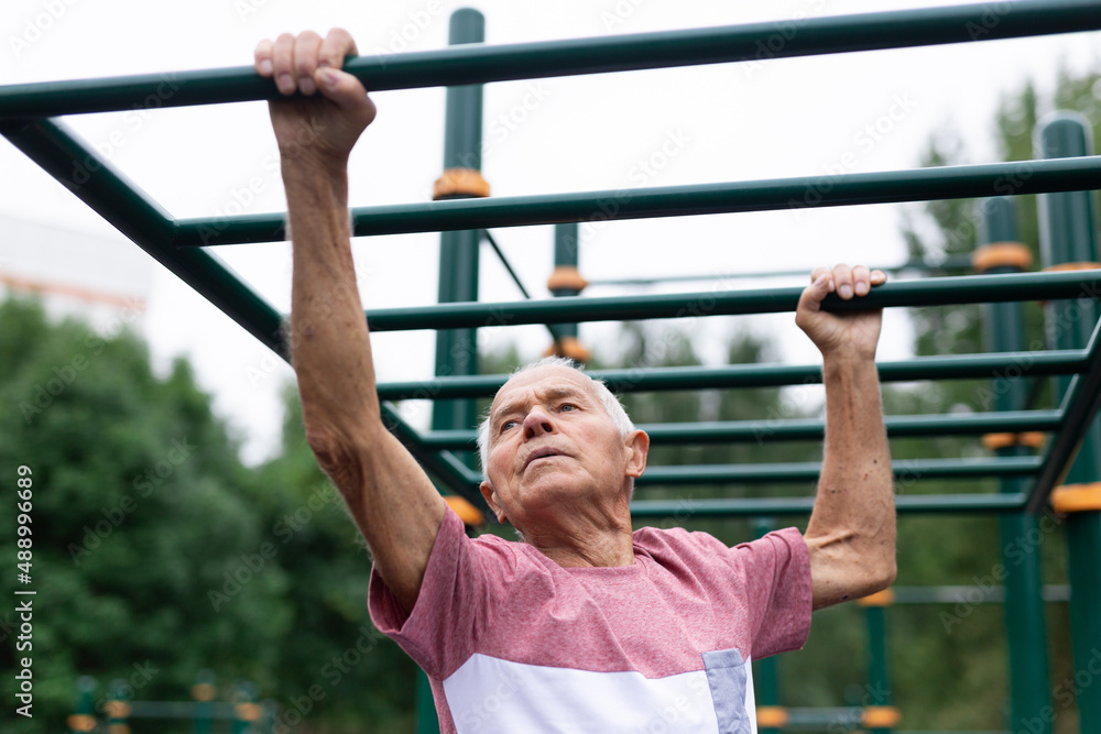 Active grandfather moves with the help of his hands on a horizontal ladder on sports ground Active grandfather moves with the help of his hands on a horizontal ladder on sports ground