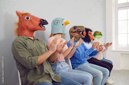 Audience in different funny bizarre silly animal masks applauding at interesting lecture or workshop. Group of happy foolish people with horse, bird, dino, ape and frog faces clapping hands at seminar photo