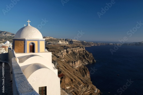 An alley with a beautiful and colorful Greek chapel next to the aegean sea in Fira Santorini