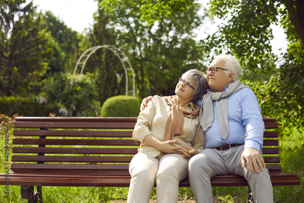 Romantic loving senior elderly european couple family sitting on bench and hugging rest on weekend in green city park outdoors. Happy retirement, healthy lifestyle on pension concept Romantic loving senior elderly european couple family sitting on bench and hugging rest on weekend in green city park outdoors. Happy retirement, healthy lifestyle on pension concept