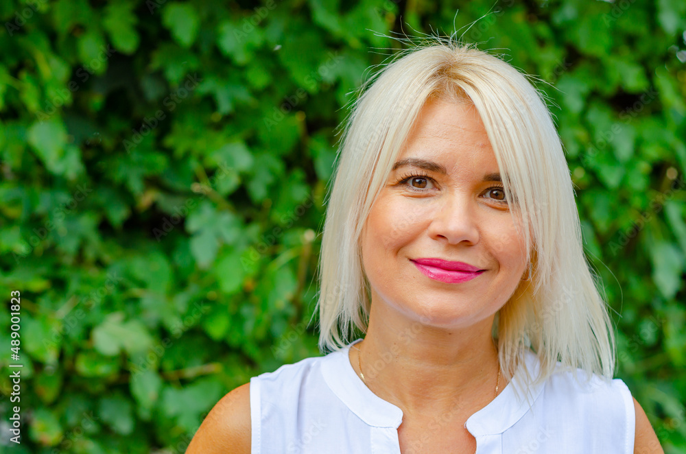 Portrait of a tanned middle-aged woman. Bright makeup. Blonde. Blurred greens background. Portrait of a tanned middle-aged woman. Bright makeup. Blonde. Blurred greens background.