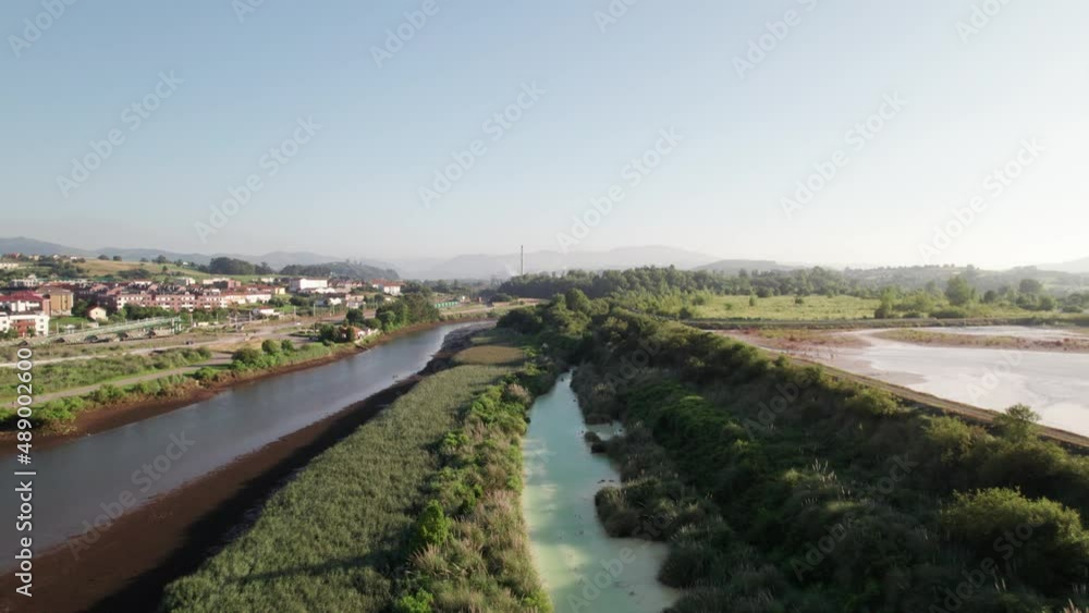 Calm river between the vast nature and small Spanish village in the province of Catabria on a warm summer day. Low angle drone dolley shot Calm river between the vast nature and small Spanish village in the province of Catabria on a warm summer day. Low angle drone dolley shot