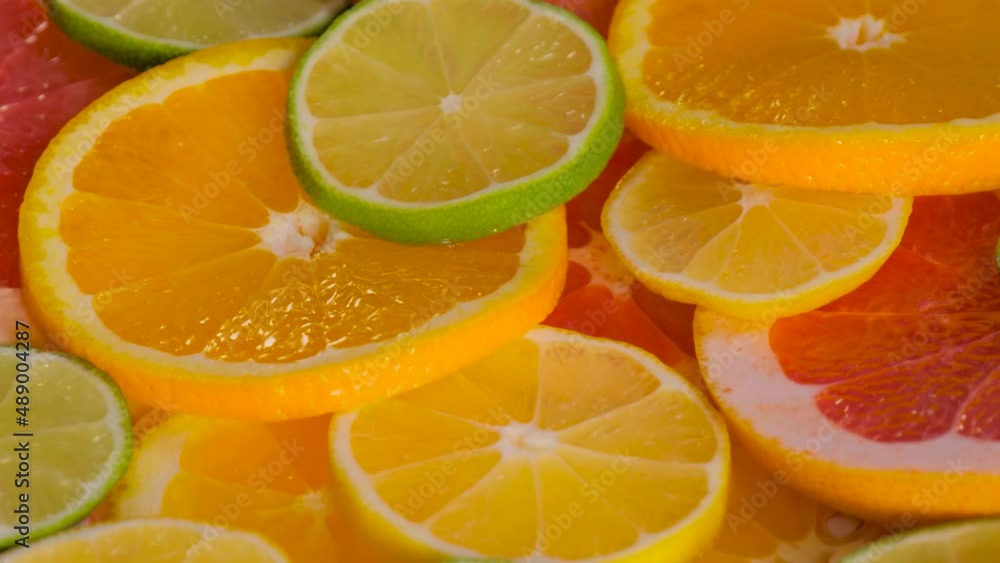 Close up view: colorful fresh citrus fruit slices - orange, grapefruit, lemon and lime on slow rotating surface - selective focus. Summer, tropical, natural, exotic and healthy food concept Close up view: colorful fresh citrus fruit slices - orange, grapefruit, lemon and lime on slow rotating surface - selective focus. Summer, tropical, natural, exotic and healthy food concept
