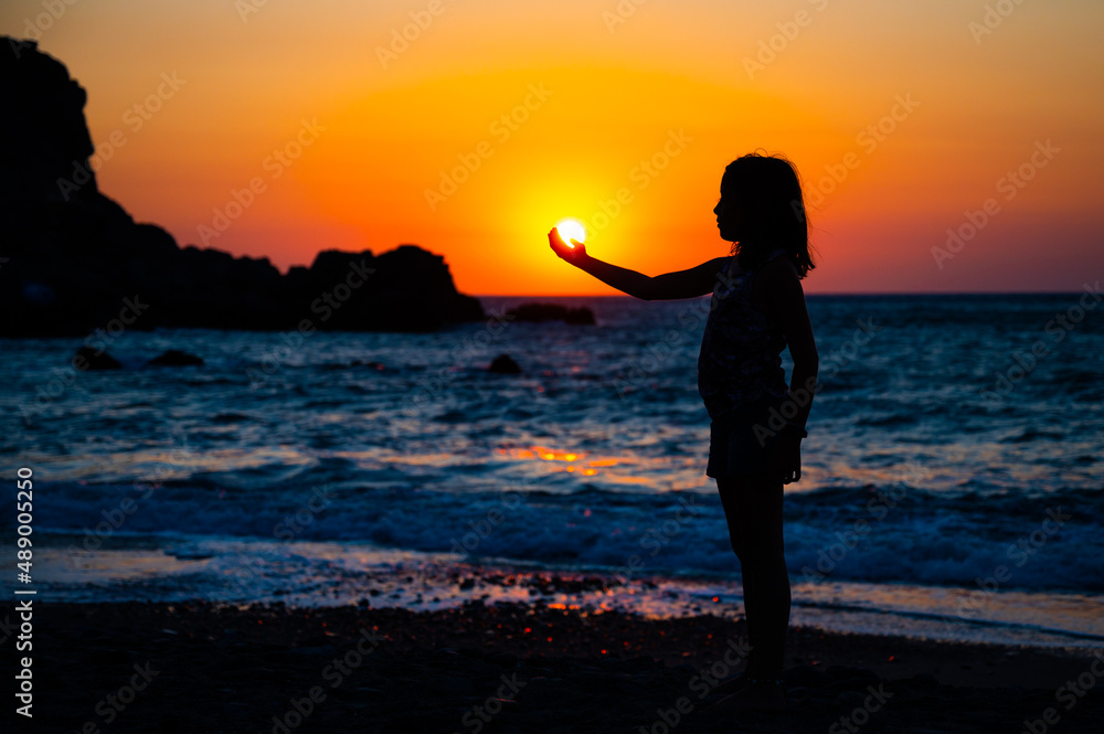Fototapeta premium Silhouette of a child holding sun in hand on a beach.