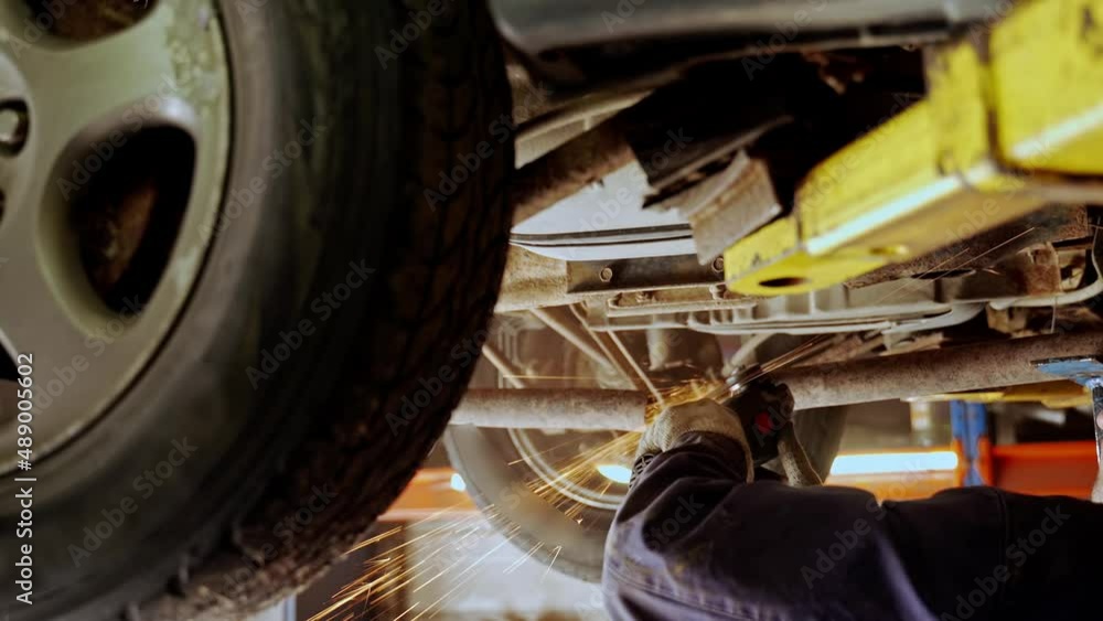 custom made wallpaper toronto digitala man cuts a muffler pipe with an angle grinder. a worker in a uniform under the bottom of a car on a lift