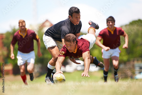 This game is not for the faint hearted. Full length shot of a young rugby player scoring a try mid tackle. © Cameron Mcdonald/peopleimages.com