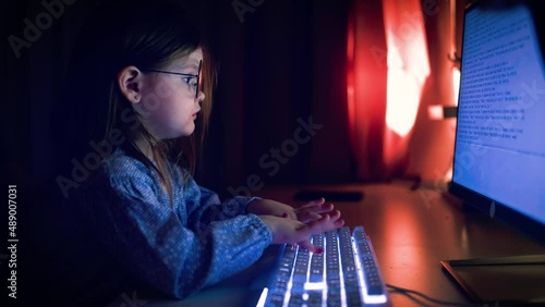 cute baby girl is typing on keybord at the computer in dark room photo