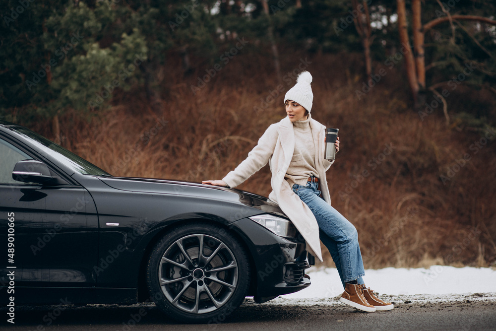 Woman in winter time sitting on car hood and drinking coffee