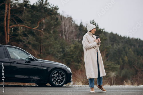 Woman drinking coffee by her car standing on the road in forest © Petro