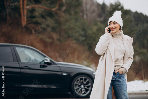 Woman talking on the phone by her car on the road in winter forest