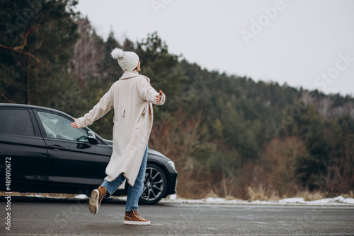 Woman walking cross the road by her car in winter forest