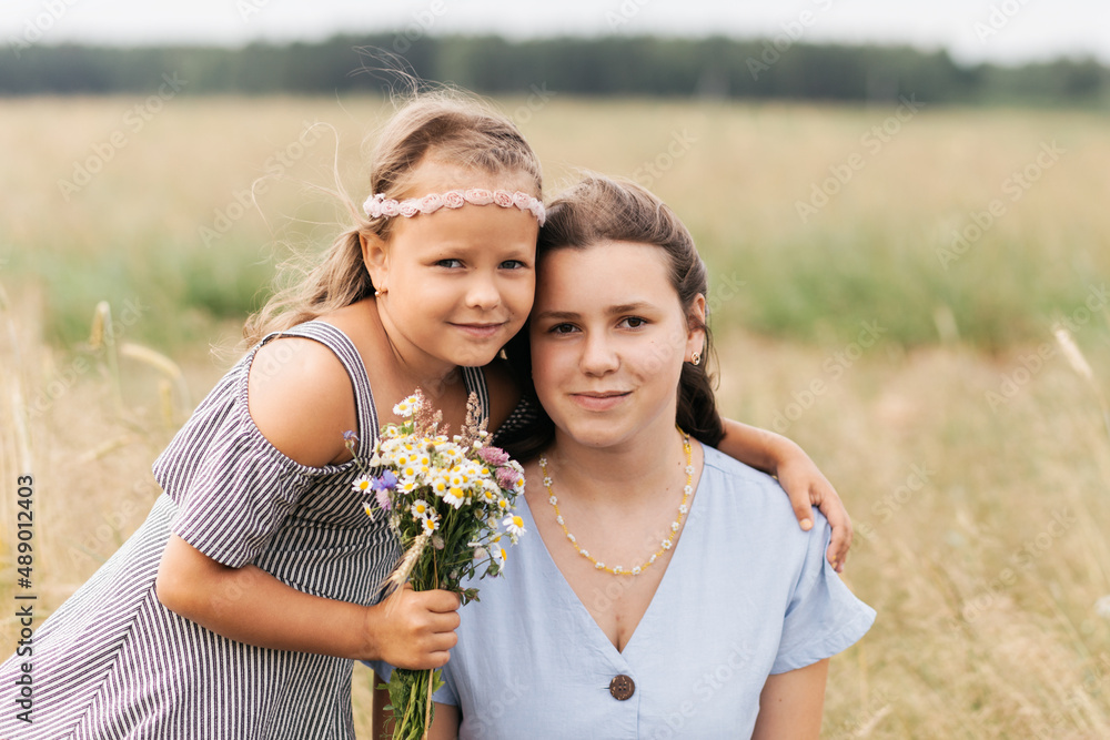 Two sisters older and younger play in the field with flowers Two sisters older and younger play in the field with flowers