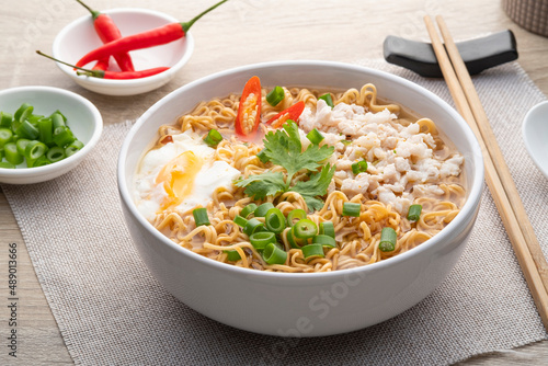Instant noodle soup with minced pork and boiled egg in white bowl on wood table