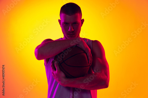 Studio shot of muscled man, basketball player, danker isolated on gradient yellow purple background in neon light. Beauty, sport, motion, activity concepts. photo