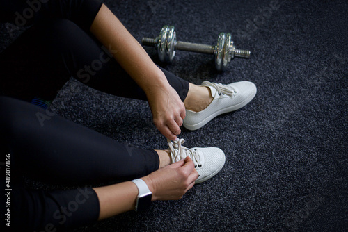 woman in the gym, sitting on a gray floor, tying her shoelaces